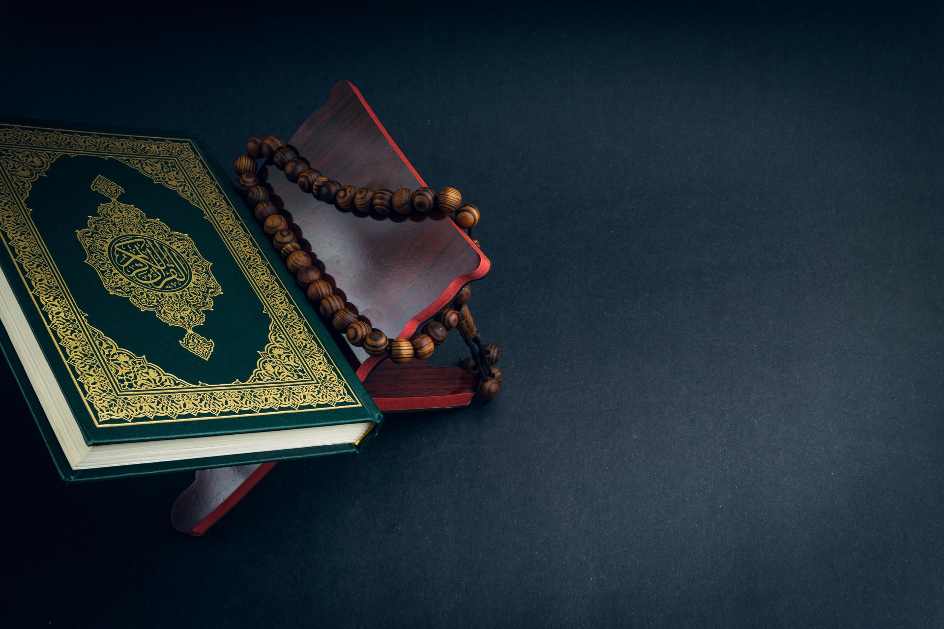 Holy Al Quran with written arabic calligraphy meaning of Al Quran and tasbih or prayer beads beads on black background
